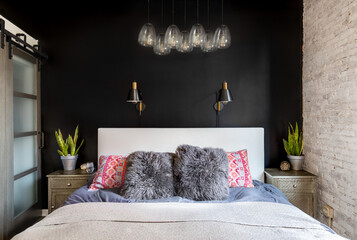 A bedroom detail with a black accent wall, black and gold lights mounted, a glass chandelier light...