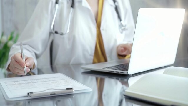 Doctor Filling Out Medical Forms While Sitting At The Glass Desk.