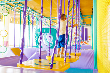 Child navigating through purple and yellow play structure in indoor playground.