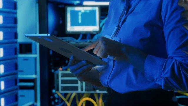 Close up shot of hands of female data center engineer using digital tablet in dark server room