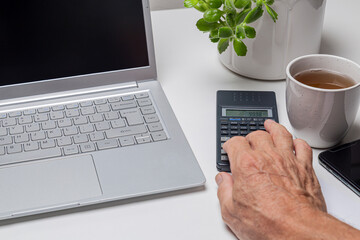 Close-up of senior man using calculator and laptop on white table
