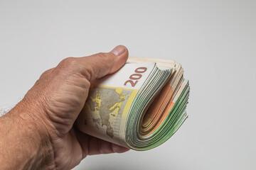 Man's hand holding a bundle of euro banknotes on white background
