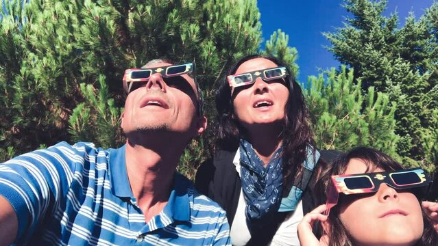 A family of three people mesmerized while watching the total solar eclipse