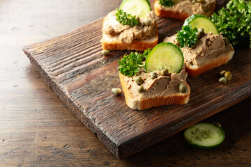  Open sandwiches with pate, cucumber, capers, and parsley on a old cutting board.