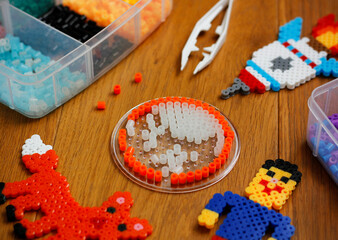 Colorful iron beads (perler beads or iron beads) in a box, art toys created from them and white...