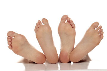 Two pairs od a beautiful well-groomed women's sole feet close-up on a white isolated studio background, The concept of foot skin care - obrazy, fototapety, plakaty