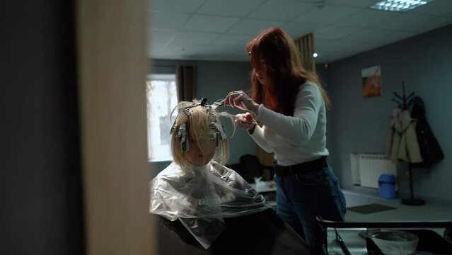 a beautiful young girl with short hair and a bob haircut is doing a procedure in a beauty salon. Hair master doing coloring and tone to client's hair close-up