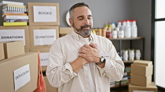 Smiling mature man with beard, standing amongst donation boxes in a warehouse as a volunteer.
