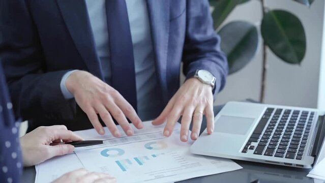 Businessman and woman analyzing data at glass desk beside a laptop in modern fair office, close up view. Business concept