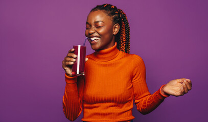 Cheerful woman enjoying a vibrant smoothie on a purple background