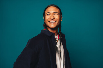 Happy ethnic man with braided hair and stylish jewelry smiling against blue background - 762681523