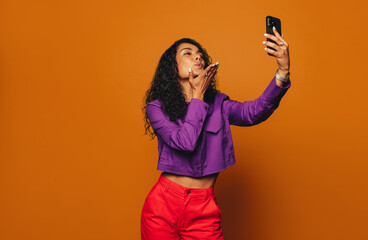 Vibrant woman taking selfie against bright orange background with modern smartphone