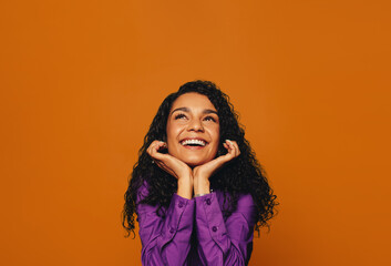 Vibrant woman with curly hair and dreamy expression smiling on colored background