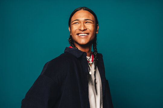 Happy ethnic man with braided hair and stylish jewelry smiling against blue background