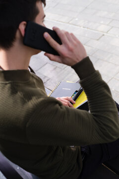 A young male student sitting on a bench and talking on a mobile phone closeup with copy space