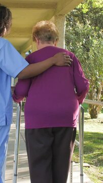 Afroamerican doctor walking with elderly woman in the hospital garden. Vertical Video