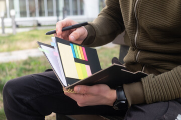 Closeup of a male person student's hands holding a notebook and writing and placing markers, college learning concept of taking notes