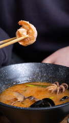 Shrimp on chopsticks on the background of tom yum soup