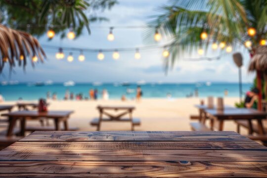 Empty wooden planks table against a blurred background with a sea coast with palm trees and glowing light bulbs in the evening