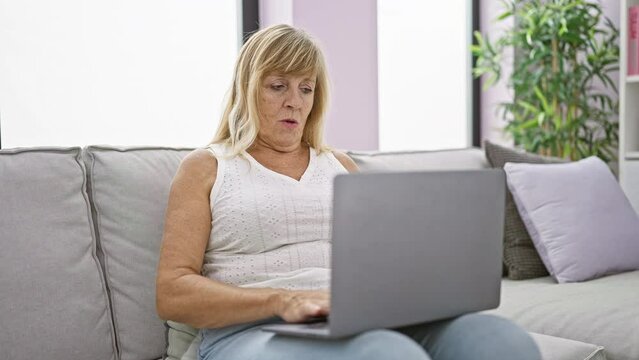 Aching tummy turns blonde, middle age woman's sofa-sitting laptop use into grueling ordeal at home.