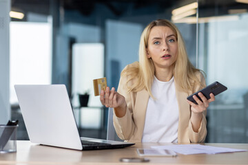 Confused woman with credit card and smartphone at desk