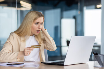 Shocked businesswoman with credit card looking at laptop