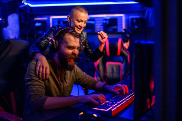 Bearded male cybersport gamer playing video game in a gameroom and celebrating