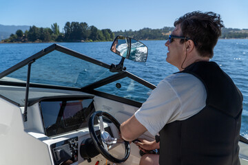 Happy man driving a speedboat on a summer day at the lake, enjoying the thrill of water sports and...