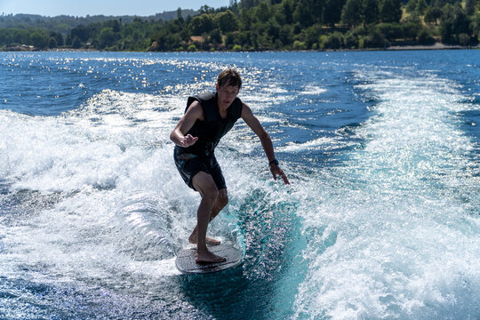 An athletic man surfing on a wakeboard in the wave on a summer day at the lake.