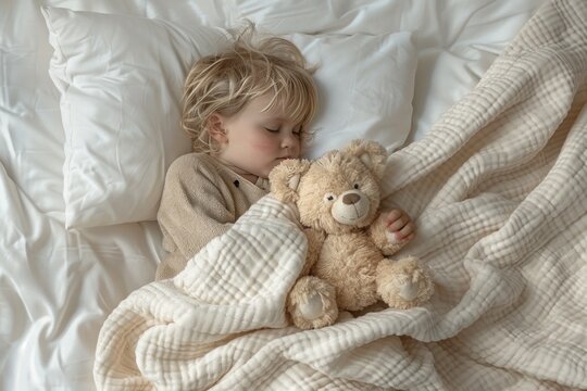 A young child is sleeping with a teddy bear. The bed is covered in a white blanket