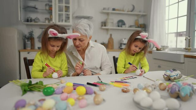 Easter grandmothers with granddaughters. Smiling grandmother with twins grandchildren painting decorating eggs in rabbit bunny ears, celebrate together at modern home. Easter family holiday concept.