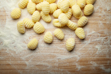 Potato gnocchi with durum wheat flour on wooden pastry board, top view, space for text, close-up.