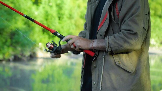 Fishing in nature with a man in a tourist robe. Men's hands hold a fishing rod.