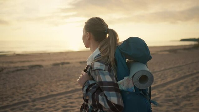 Happy woman tourist admiring sea nature. Middle aged beautiful female camper hiker carrying touristic backpack enjoying sea sunset in hike. Camping hiking travel tourism wanderlust vacations concept.