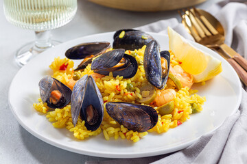 Seafood paella with mussels and shrimps, on white plate, with lemon and white wine, horizontal