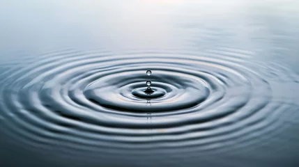  A single, pristine water drop falls into a calm pool, creating a series of perfectly symmetrical circular waves that ripple outward. © Mehram