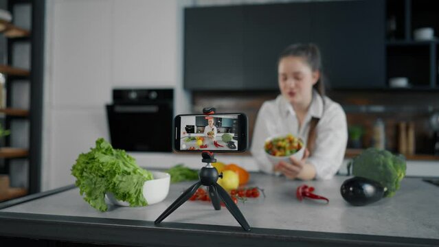 Young woman video lesson about cooking. Serious girl talks recording video lesson, filming cooks tutorial in loft kitchen studio. Concept for online healthy cooking courses, recording of training.
