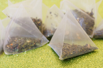 Translucent pyramid tea bags with green tea, lemon and mint slices on a shiny golden surface. The...