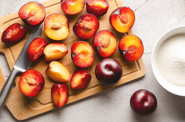 Fresh plums on cutting board with knife and sugar on grey background.