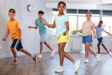 Dynamic little girl training Rock-and-Roll dance poses in dancehall with other attendees of dancing...