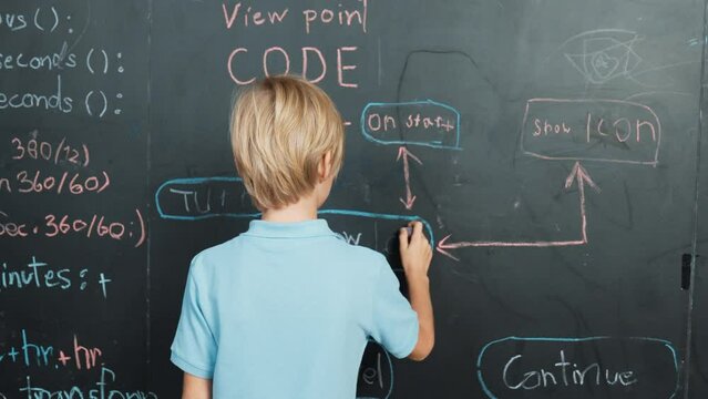 Back view of student writing engineering prompt on blackboard. Handsome clever child or boy planing a project by using coding and programing system in STEM technology classroom. Closeup. Erudition.