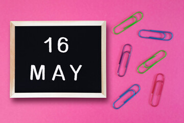 May 16 written in chalk on black board. Calendar date 16th of May on chalkboard on pink blurred school stationery background. Event schedule date. School, study, education concept. Month of spring.
