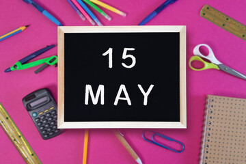 May 15 written in chalk on black board. Calendar date 15th of May on chalkboard on pink blurred school stationery background. Event schedule date. School, study, education concept. Month of spring.