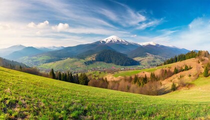 panorama of mountainous rural landscape with village in the valley carpathian countryside scenery with arable on hills in front of borzhava ridge with snow capped top on a sunny morning in spring - obrazy, fototapety, plakaty