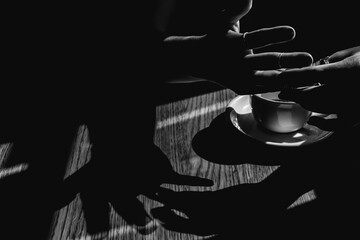 Shadows of women's hands over a wooden table and white cup of coffee. Lights and shadows in a cafe on a warm summer day. - 762757722