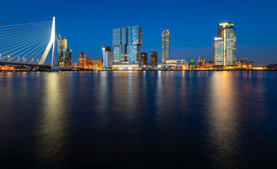 Fototapeta na wymiar Panoramic view of Rotterdam night time skyline with modern buildings and iconic bridge. Evening sky reflection in River Maas at blue hour with colorful illumination. Major port and big dutch metropole