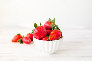 Fresh strawberries in a bowl on white wooden background. Top view with space. Nature fruit concept and healty eating.