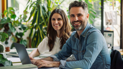Fototapeta premium A man and woman in their thirties collaborate with smiles on an online project at a laptop in a modern office with white walls and glass windows.