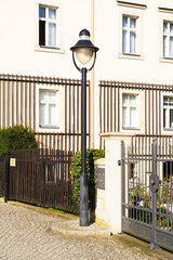 A house with a fence and a street light in front of it, located in a residential area. The buildings facade features windows and a lamp post as a fixture