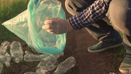 Group of people are cleaning up plastic garbage in park on grass. Hand of volunteer picks up...